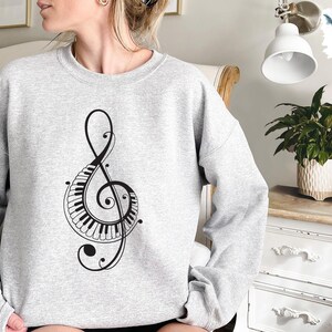 Peut inclure: Un sweat-shirt gris avec un motif de cl&eacute; de sol noire avec un clavier de piano. La cl&eacute; de sol est entour&eacute;e de volutes d&eacute;coratives.