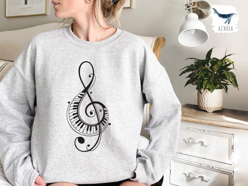 Peut inclure: Un sweat-shirt gris avec un motif de cl&eacute; de sol noire avec un clavier de piano. La cl&eacute; de sol est entour&eacute;e de volutes d&eacute;coratives.