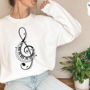 Peut inclure: Sweat-shirt blanc avec un graphique noir d'une cl&eacute; de sol avec des touches de piano int&eacute;gr&eacute;es au design.
