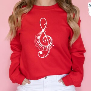 Peut inclure: Un sweat-shirt rouge avec un motif de cl&eacute; de sol blanche orn&eacute; d'un clavier de piano. Le motif est complexe et d&eacute;taill&eacute;.
