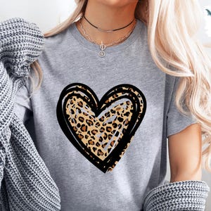 Puede incluir: Una camiseta gris con un dise&ntilde;o de coraz&oacute;n de estampado de leopardo negro y marr&oacute;n.