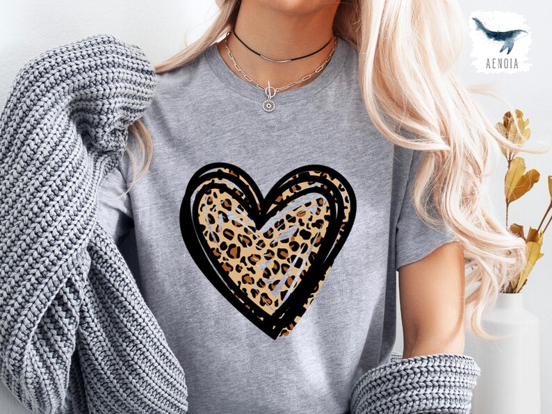 Puede incluir: Una camiseta gris con un dise&ntilde;o de coraz&oacute;n de estampado de leopardo negro y marr&oacute;n.