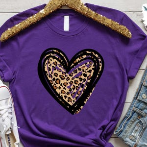 Puede incluir: Camiseta morada con un contorno negro y blanco de un coraz&oacute;n relleno de un estampado de leopardo.