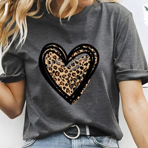 Puede incluir: Una camiseta gris con un dise&ntilde;o de coraz&oacute;n de estampado de leopardo negro y marr&oacute;n.