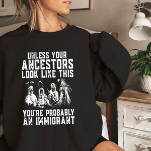 May include: Black sweatshirt with white text that reads "Unless your ancestors look like this you're probably an immigrant". The text is surrounded by an illustration of four Native American people.