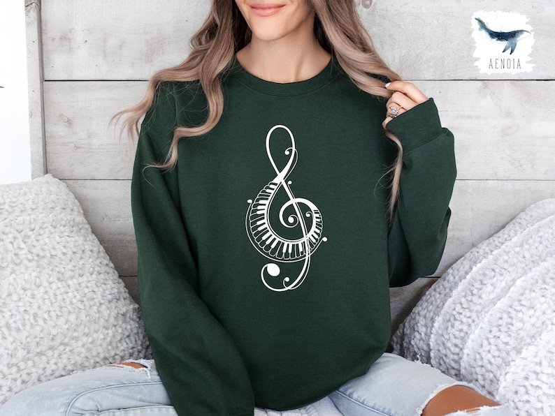 Peut inclure: Un sweat-shirt vert fonc&eacute; avec un motif de cl&eacute; de sol blanche. La cl&eacute; de sol est compos&eacute;e de touches de piano et de volutes.