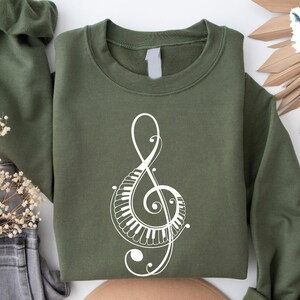 Peut inclure: Un sweat-shirt vert avec un motif de cl&eacute; de sol blanche. La cl&eacute; de sol est compos&eacute;e de touches de piano.