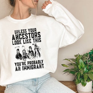 May include: White sweatshirt with a black graphic print that reads "Unless your ancestors look like this you're probably an immigrant". The graphic features a group of four Native American people.