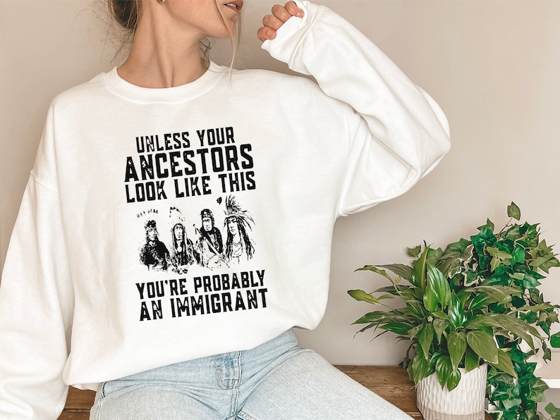 May include: White sweatshirt with a black graphic print that reads "Unless your ancestors look like this you're probably an immigrant". The graphic features a group of four Native American people.