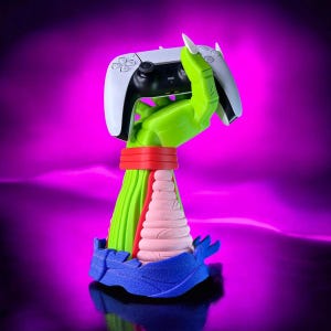 May include: A green hand holding a white and black video game controller. The hand is attached to a multi-colored base with a blue, pink, and green design.