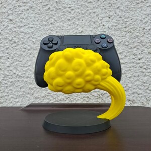 May include: A black video game controller sits on a yellow 3D printed stand shaped like a cloud. The stand has a round base.