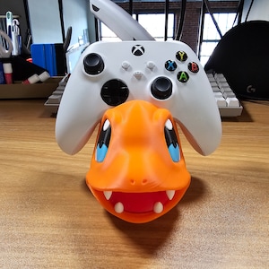 May include: A white Xbox controller with orange and blue accents sits on top of an orange and blue Pokemon Charmander figure.