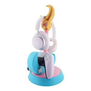 May include: A colorful headset and controller stand. The stand is primarily light blue, pink, and gold, with a star and crescent moon design. A white headset and controller are displayed on the stand.