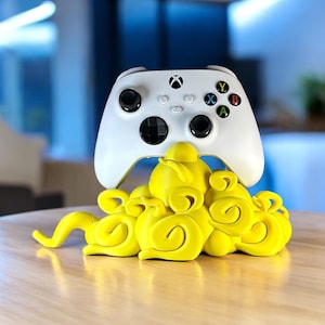 May include: A white Xbox controller rests on a bright yellow, cloud-shaped stand. The controller has black buttons and colored action buttons. The stand is a decorative accessory for gaming enthusiasts.