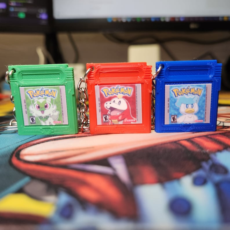 May include: Three green, red, and blue Pokemon Game Boy Color keychains. Each keychain features a different Pokemon character and the text "Pokemon" on the front.
