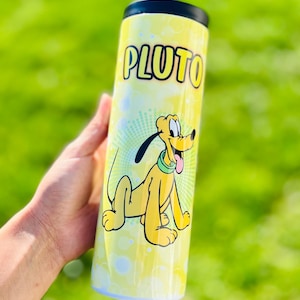 May include: A yellow tumbler featuring Pluto, the Disney cartoon dog. The word "PLUTO" is printed in large, black letters above the character. Pluto is depicted in a seated position with his tongue sticking out. The tumbler has a black lid.