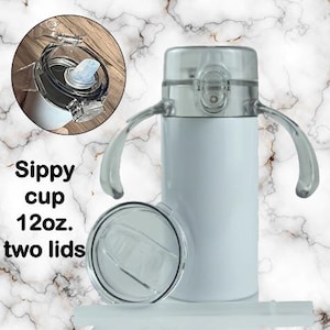Puede incluir: Vaso con boquilla blanco con dos tapas transparentes y asas. El vaso tiene una capacidad de 355 ml. La imagen tambi&eacute;n muestra un primer plano de la tapa y el texto "Sippy cup 12oz. two lids."