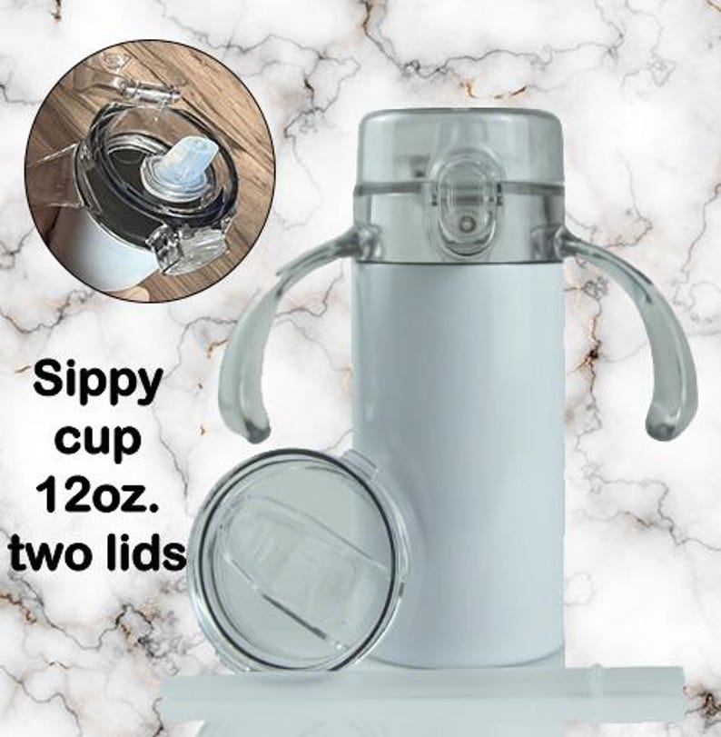 Puede incluir: Vaso con boquilla blanco con dos tapas transparentes y asas. El vaso tiene una capacidad de 355 ml. La imagen tambi&eacute;n muestra un primer plano de la tapa y el texto "Sippy cup 12oz. two lids."