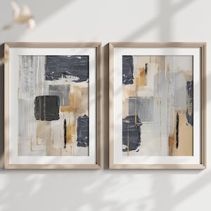 Könnte beinhalten: Zwei gerahmte abstrakte Gemälde mit einem geometrischen Design in Grautönen, Beige und Gold. Die Gemälde hängen an einer weißen Wand.