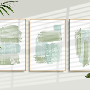 以下が含まれることがあります： 緑と青の水彩画のデザインが施された、額装された抽象的なアートプリントが3枚。プリントはシンプルな木製フレームに入っていて、白い壁に掛けられています。