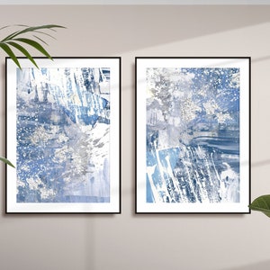 May include: Two framed abstract art prints with a blue, white and grey colour scheme. The prints feature a textured, brushstroke style.