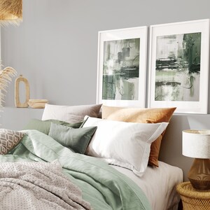 May include: A bedroom with a green and white bedding set, two framed abstract paintings with green and white brushstrokes, a wooden nightstand with a lamp, and a woven basket.