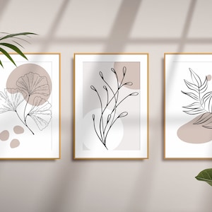 May include: Three framed prints featuring minimalist line drawings of leaves and branches on a light beige background. The frames are gold and the prints are arranged in a row.