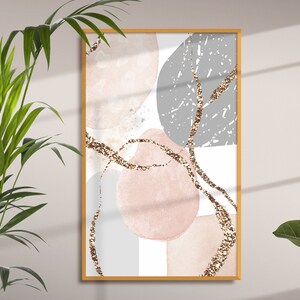 K&ouml;nnte beinhalten: Abstrakter Kunstdruck mit rosa, grauen und wei&szlig;en Formen und goldenen Glitzerakzenten. Der Druck ist in einem hellen Holzrahmen gerahmt.