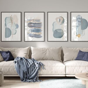 Op de afbeelding: Set van vier abstracte kunstprints met blauwe en gouden geometrische vormen op een witte achtergrond. De prints zijn in zwart ingelijst en hangen aan een grijze muur boven een witte bank.