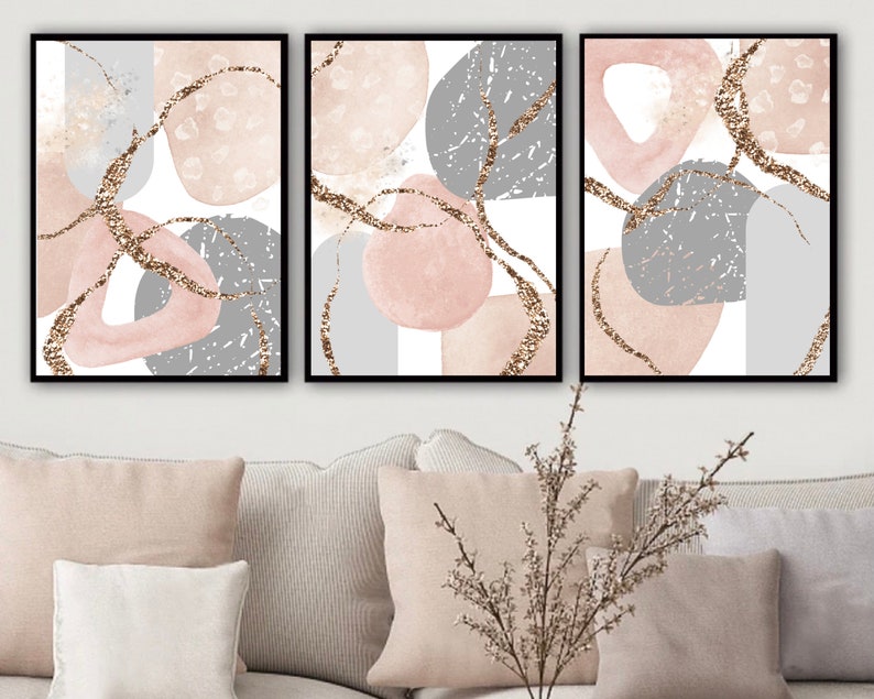 K&ouml;nnte beinhalten: Drei abstrakte Kunstdrucke mit rosa und grauen Formen und goldenen Glitzerakzenten. Die Drucke sind in Schwarz gerahmt und haben einen wei&szlig;en Hintergrund.