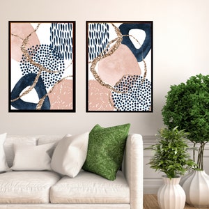 May include: Two framed abstract art prints. Each print features navy blue, blush pink, and gold glitter accents on a white background. The designs include geometric shapes and dotted patterns. The frames are black.