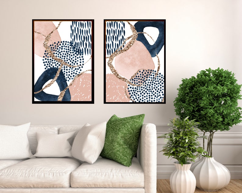 May include: Two framed abstract art prints. Each print features navy blue, blush pink, and gold glitter accents on a white background. The designs include geometric shapes and dotted patterns. The frames are black.