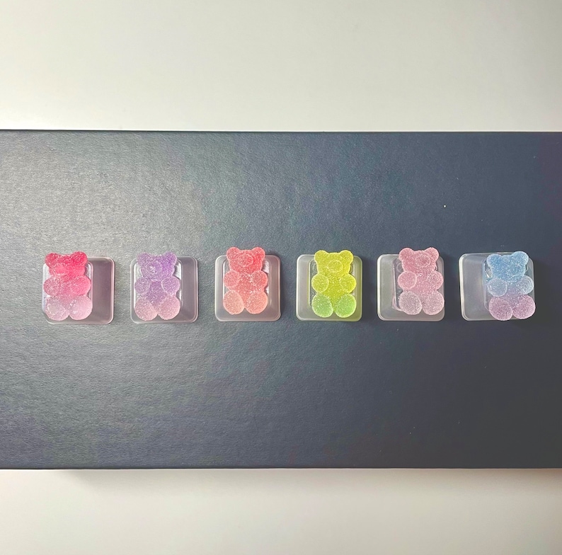 Pode incluir: Seis balas de goma em forma de urso em recipientes de pl&aacute;stico transparente. Os ursos de goma s&atilde;o de um arco-&iacute;ris de cores: rosa, roxo, azul claro, verde, amarelo e azul.