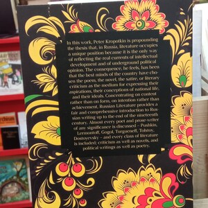 May include: A book with a black cover featuring a traditional floral design in yellow, red, and green. The back cover includes text discussing Russian literature and its significance. The book is part of a collection.