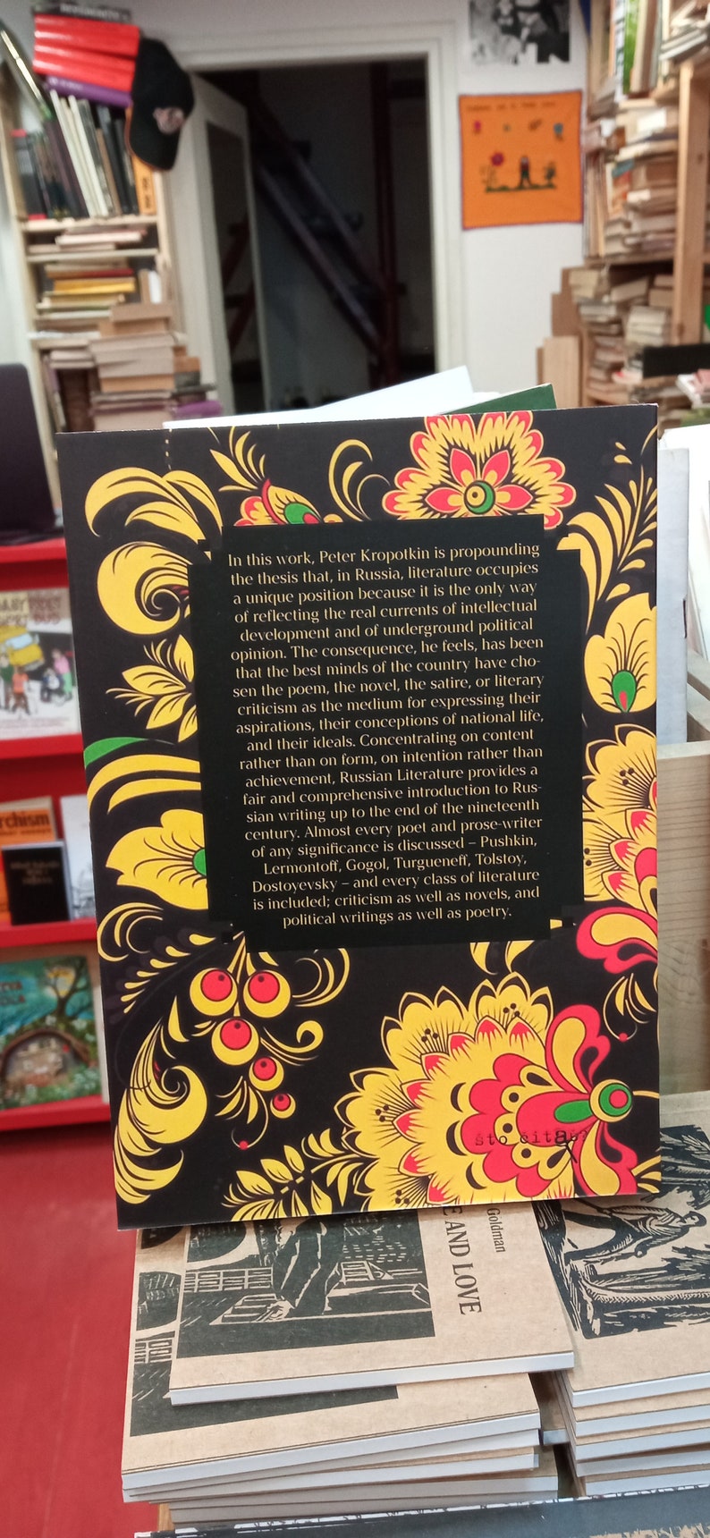 May include: A book with a black cover featuring a traditional floral design in yellow, red, and green. The back cover includes text discussing Russian literature and its significance. The book is part of a collection.