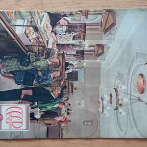 Puede incluir: Portada de revista vintage con una fotografía de personas en una tienda, posiblemente una panadería o un mercado. La portada tiene un logotipo rojo y blanco con el año 1946. El fondo es una superficie de madera.