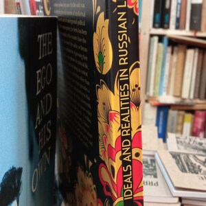 May include: A hardcover book titled "Ideals and Realities in Russian Literature" by Peter Kropotkin. The book has a black cover with a floral design in red, yellow, and gold. The spine displays the title vertically.