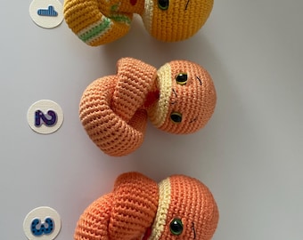 May include: Three crocheted snake toys. The first snake is yellow with green stripes and a yellow head. The second snake is orange with a yellow head. The third snake is orange with a yellow head.