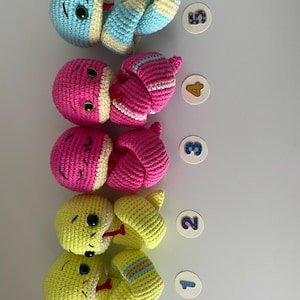 May include: Five crocheted snake toys in different colors. The snakes are curled up and have cute faces. The snakes are numbered 1 through 5.