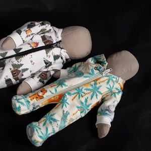 May include: Two handmade cloth dolls wearing pajamas. One doll is wearing white pajamas with a green and brown camping print. The other doll is wearing white pajamas with a green and yellow palm tree print.