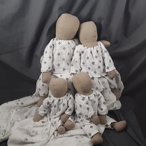 Puede incluir: Cuatro muñecas de tela que llevan pijamas blancos con un patrón geométrico azul y blanco. Las muñecas están sentadas en una manta blanca con un patrón de estrellas azules y blancas.