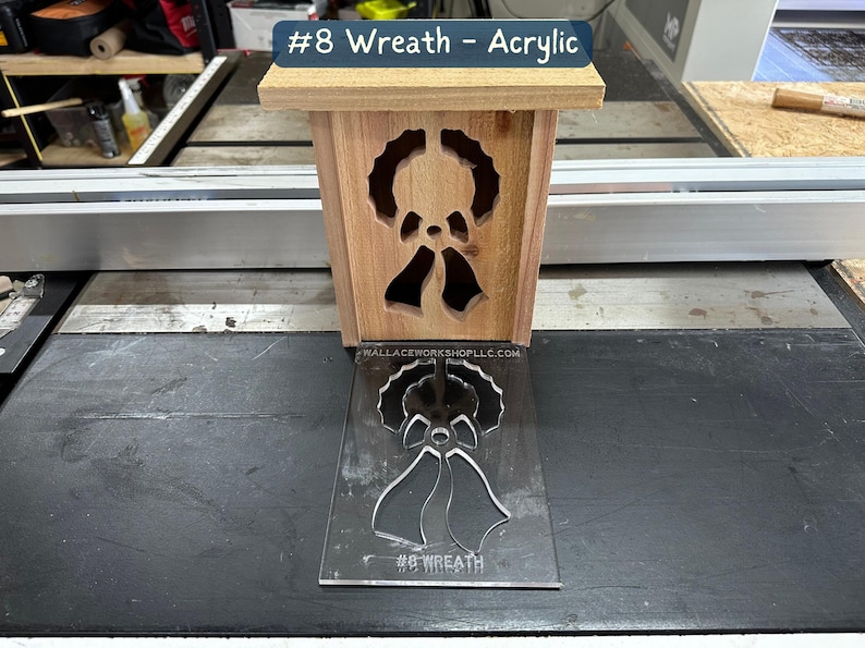 May include: A wooden box with a cut-out design of a wreath and bells. The box is sitting on a black surface next to a clear acrylic stencil with the same design. The stencil has the text "#8 Wreath" printed on it.