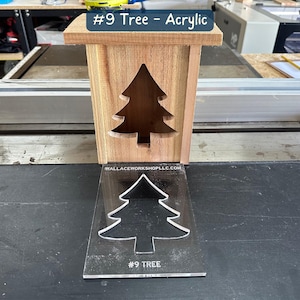 May include: A wooden box with a cutout of a Christmas tree. The box is sitting on a table next to a clear acrylic sheet with a tree cutout and the text "#9 TREE".