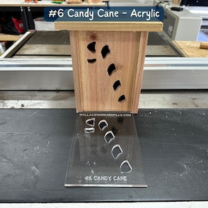 May include: A wooden box with a candy cane design cut out. The box is sitting on a black surface with a clear acrylic sheet that has the same candy cane design cut out. The acrylic sheet has the text "#6 Candy Cane" printed on it.