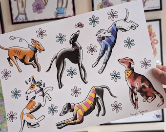 May include: A white art print featuring six greyhound dogs in various poses and outfits, including sweaters and bandanas, surrounded by small blue and pink flower illustrations. The bottom right corner contains the handwritten text Snips Tattoos.