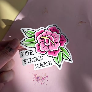 May include: A die-cut sticker featuring a pink rose with green leaves and yellow accents. The text "SNIPS TATTOOS" is printed on a leaf, and the words "FOR FUCKS SAKE" are written in black, bold, stylized lettering below the flower.