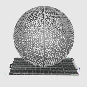 May include: A gray, spherical, 3D printed object with a honeycomb pattern. The object is sitting on a gray, textured surface.