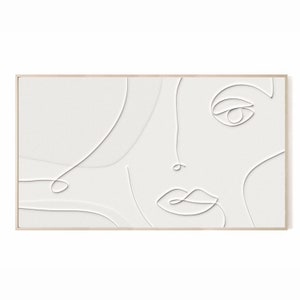 May include: White abstract face art print in a light wood frame. The artwork features a minimalist line drawing of a face, with delicate lines forming the features against a textured white background. A modern piece for home decor.