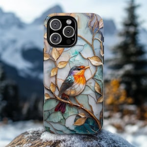 May include: A phone case featuring a colorful bird perched on a branch with gold-colored leaves. The bird has orange, red, blue, and white feathers. The background is a mosaic-like design with shades of blue and green.