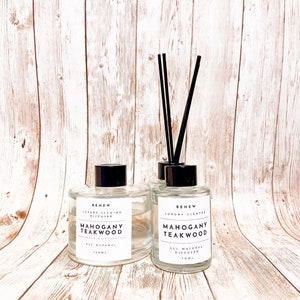 May include: Two clear glass bottles with black lids and black diffuser sticks. The bottles are labeled "BENEW LUXURY SCENTED DIFFUSER MAHOGANY TEAKWOOD ALL NATURAL 150ML" and "BENEW LUXURY SCENTED MAHOGANY TEAKWOOD ALL NATURAL DIFFUSER 10ML".